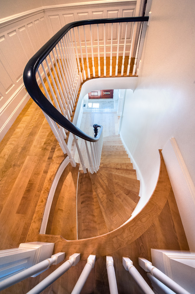 Imagen de escalera curva clásica grande con escalones de madera y contrahuellas de madera pintada