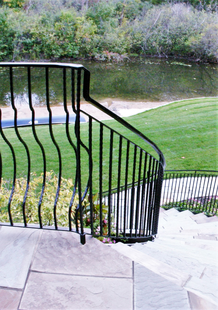 Imagen de escalera curva clásica grande con escalones de pizarra, contrahuellas de metal y barandilla de metal