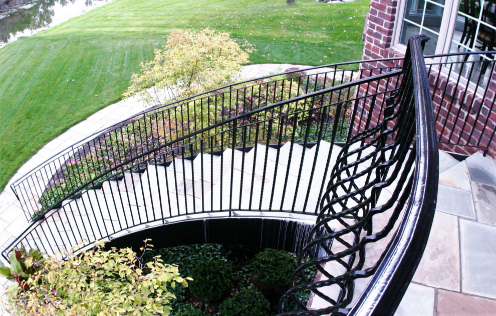 На фото: большая изогнутая металлическая лестница в классическом стиле с ступенями из сланца и металлическими перилами с
