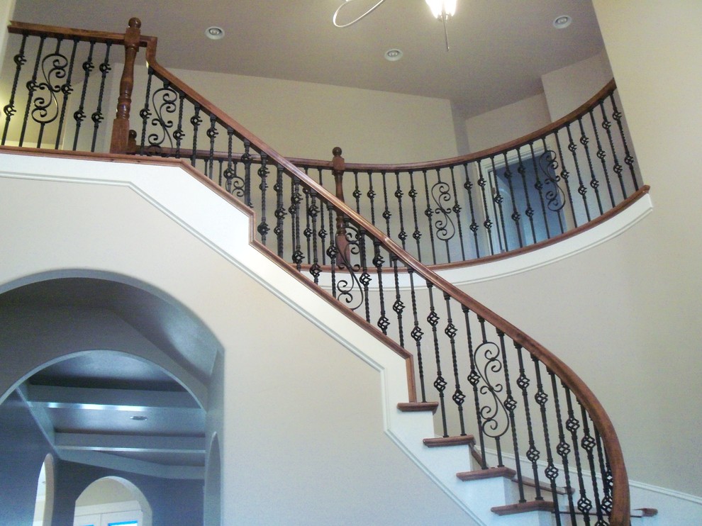 Cette image montre un grand escalier peint courbe traditionnel avec des marches en bois et un garde-corps en métal.