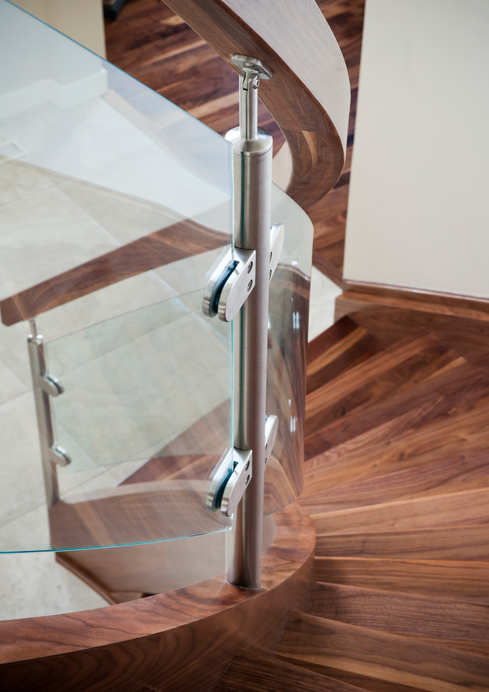 Réalisation d'un escalier courbe minimaliste avec des marches en bois, des contremarches en bois et un garde-corps en verre.
