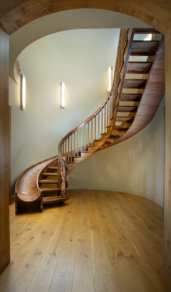 Идея дизайна: огромная изогнутая лестница в стиле фьюжн с деревянными ступенями и деревянными перилами без подступенок