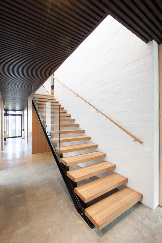 Ejemplo de escalera suspendida industrial grande sin contrahuella con escalones de madera y barandilla de vidrio