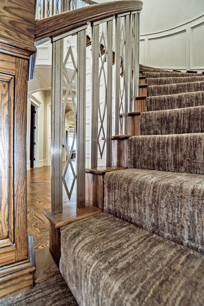 На фото: огромная изогнутая лестница в классическом стиле с ступенями с ковровым покрытием, ковровыми подступенками и перилами из смешанных материалов с
