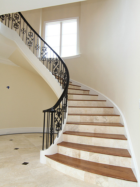 Пример оригинального дизайна: большая изогнутая лестница в классическом стиле с деревянными ступенями, подступенками из известняка и металлическими перилами