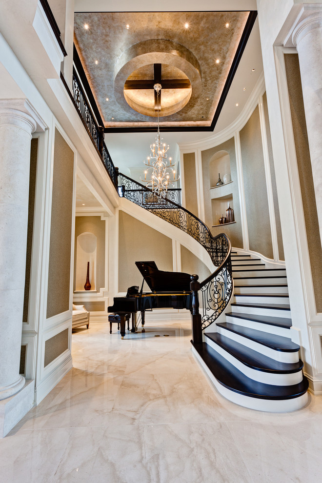 На фото: огромная изогнутая лестница в классическом стиле с деревянными ступенями, крашенными деревянными подступенками и металлическими перилами