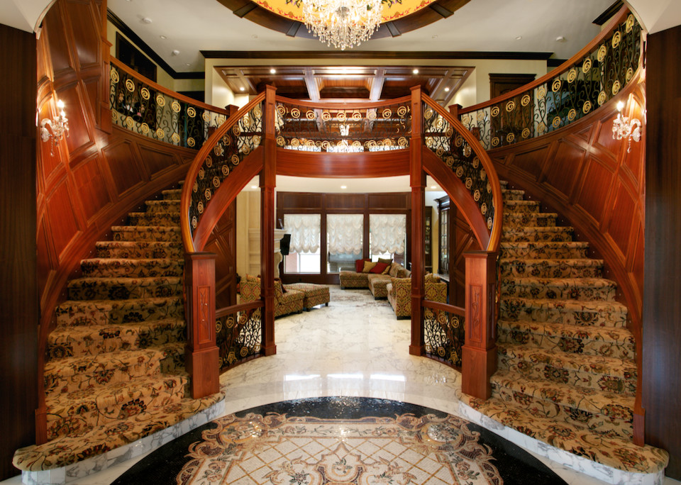 Пример оригинального дизайна: огромная изогнутая лестница в восточном стиле с ступенями с ковровым покрытием, ковровыми подступенками и перилами из смешанных материалов