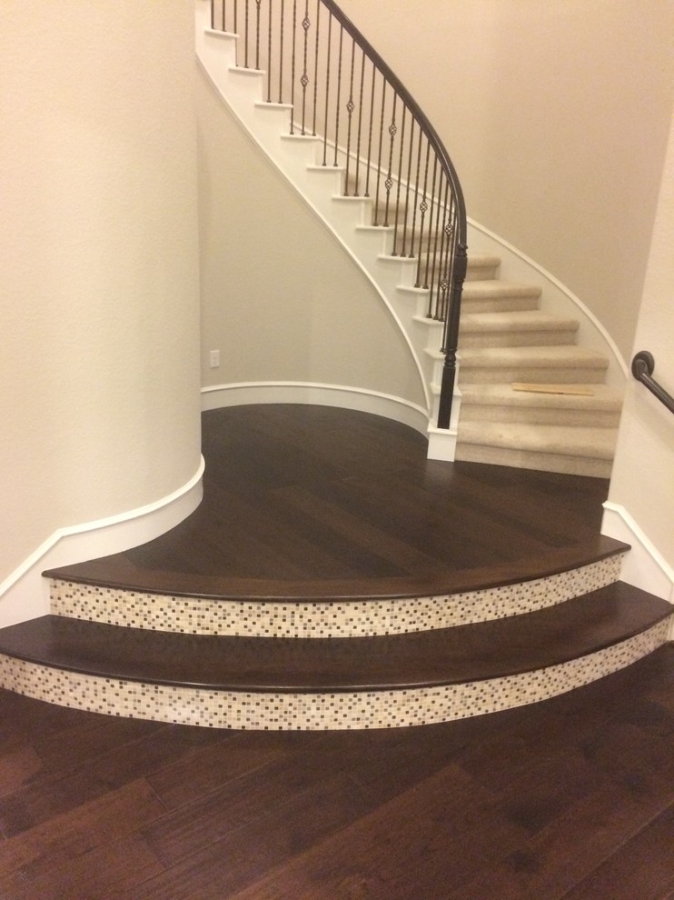 Modelo de escalera curva clásica renovada grande con escalones de madera, contrahuellas con baldosas y/o azulejos y barandilla de metal