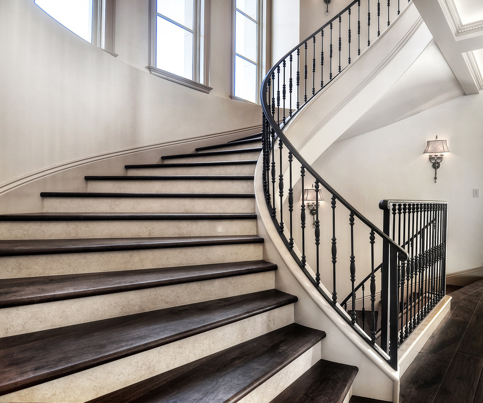 На фото: большая изогнутая лестница в классическом стиле с деревянными ступенями и крашенными деревянными подступенками