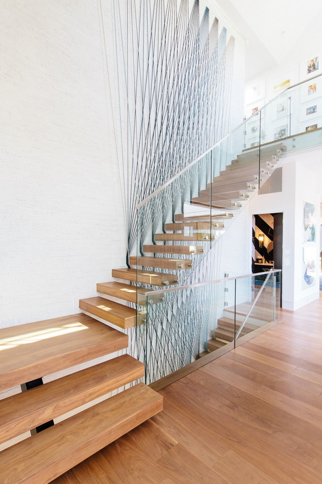 Aménagement d'un grand escalier contemporain en L avec des marches en bois, des contremarches en verre et un garde-corps en verre.