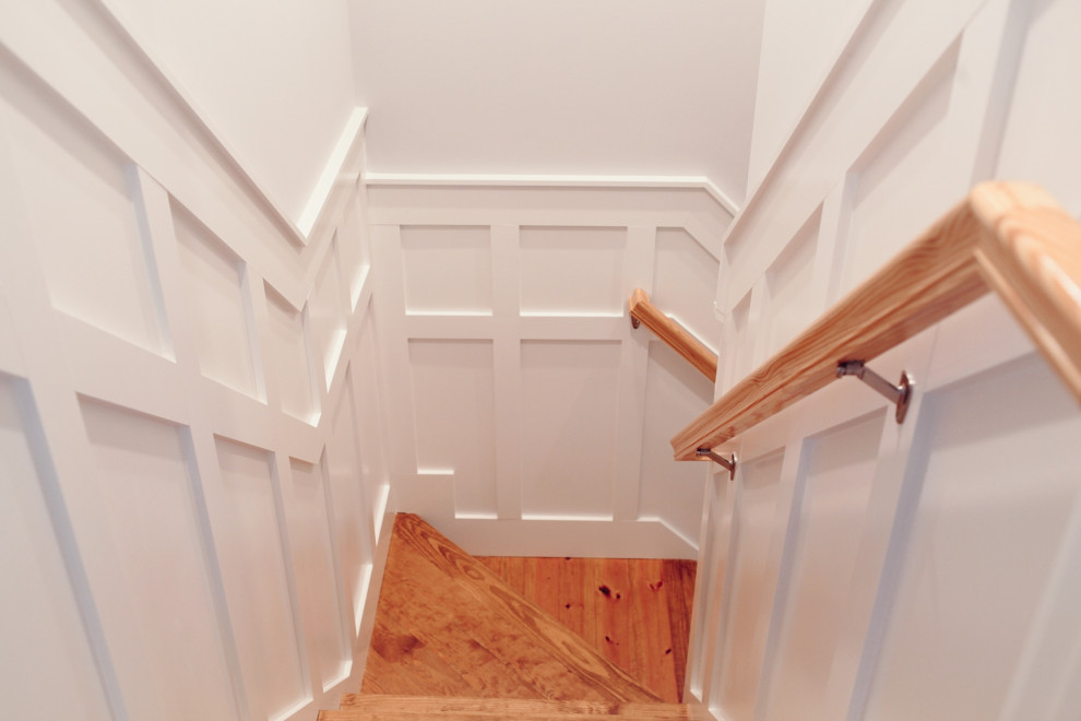 На фото: угловая лестница в стиле кантри с деревянными ступенями, деревянными перилами и панелями на части стены с