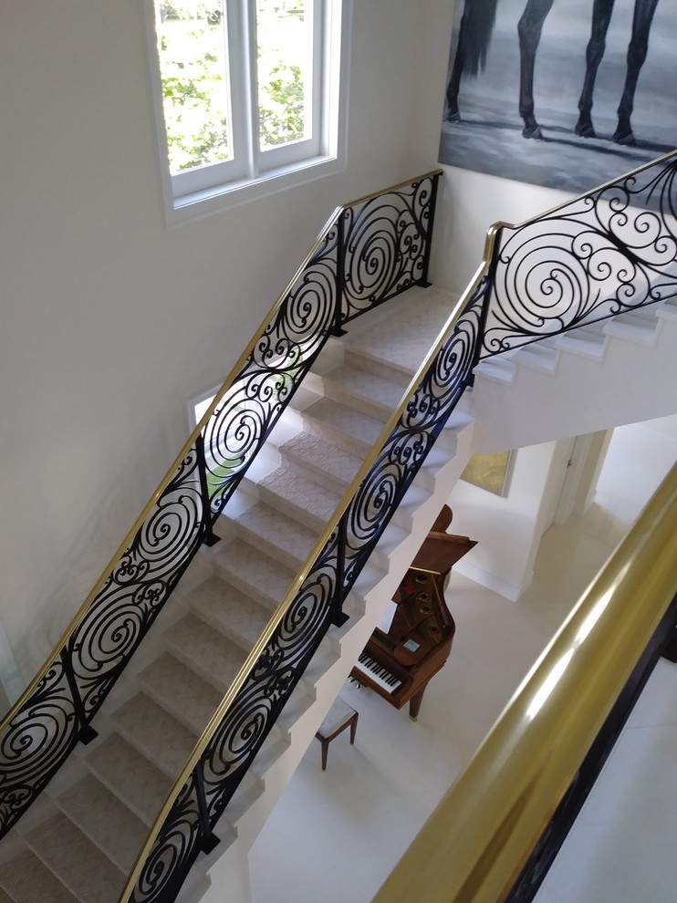 Стильный дизайн: большая угловая лестница в современном стиле с мраморными ступенями, подступенками из мрамора и металлическими перилами - последний тренд
