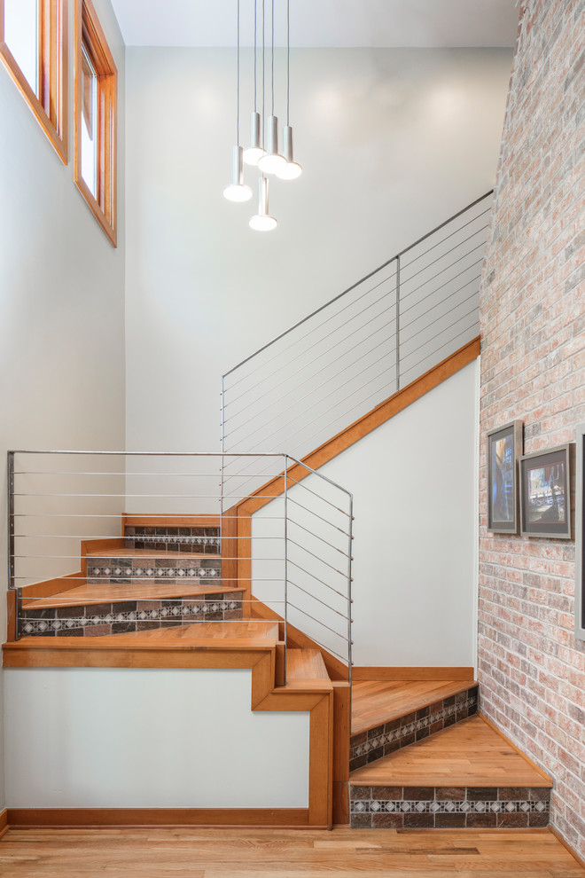 Foto de escalera contemporánea con contrahuellas con baldosas y/o azulejos, barandilla de metal y escalones de madera