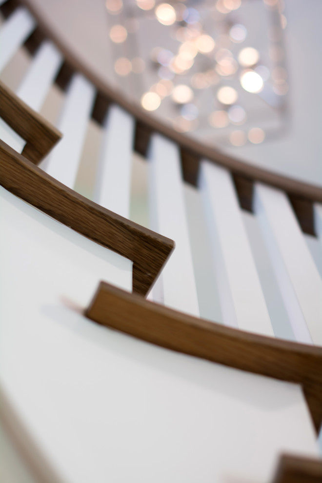 Пример оригинального дизайна: большая изогнутая лестница в стиле неоклассика (современная классика) с ступенями с ковровым покрытием, ковровыми подступенками и деревянными перилами