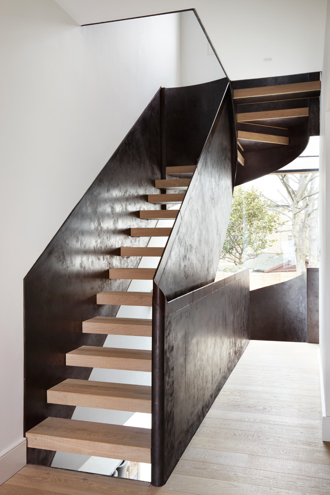 Bild på en stor funkis svängd trappa i trä, med öppna sättsteg och räcke i metall