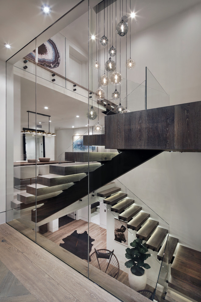 Cette image montre un escalier sans contremarche design en U avec des marches en bois, un garde-corps en verre et éclairage.