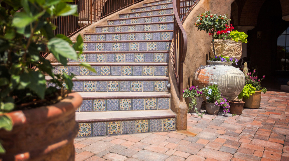 Diseño de escalera curva mediterránea grande con escalones de hormigón, contrahuellas con baldosas y/o azulejos y barandilla de metal