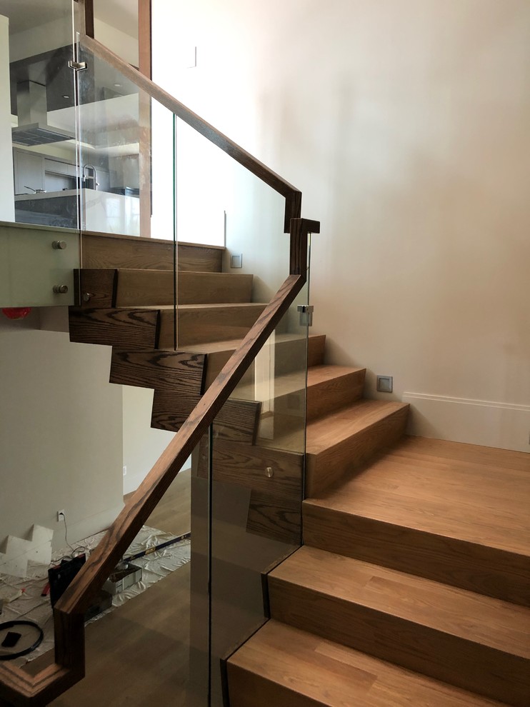 Cette photo montre un escalier moderne en U de taille moyenne avec des marches en bois, des contremarches en bois et un garde-corps en verre.