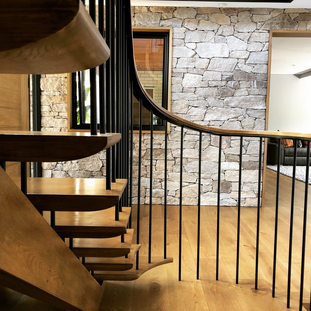 Стильный дизайн: большая изогнутая лестница в стиле ретро с деревянными ступенями, металлическими перилами и панелями на стенах без подступенок - последний тренд