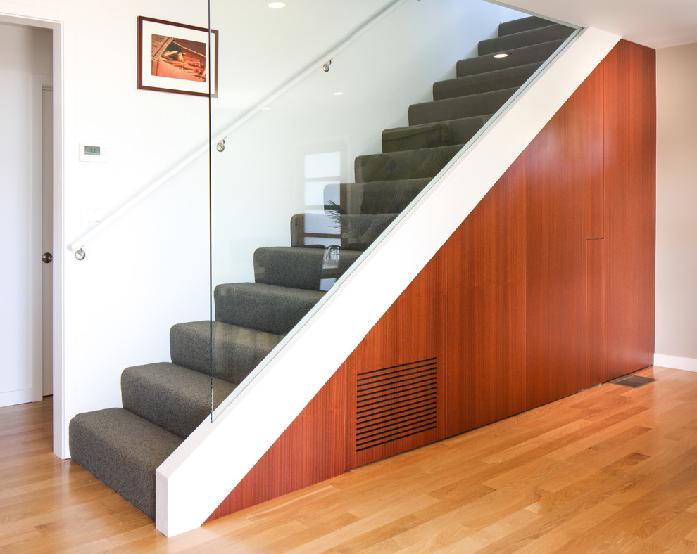 Idée de décoration pour un grand escalier droit design avec des marches en moquette, des contremarches en moquette et un garde-corps en verre.