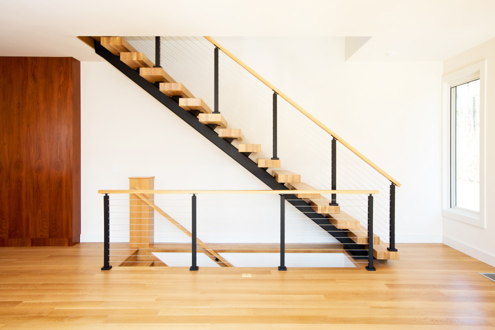 Exempel på en stor modern flytande trappa i trä, med sättsteg i trä och räcke i flera material