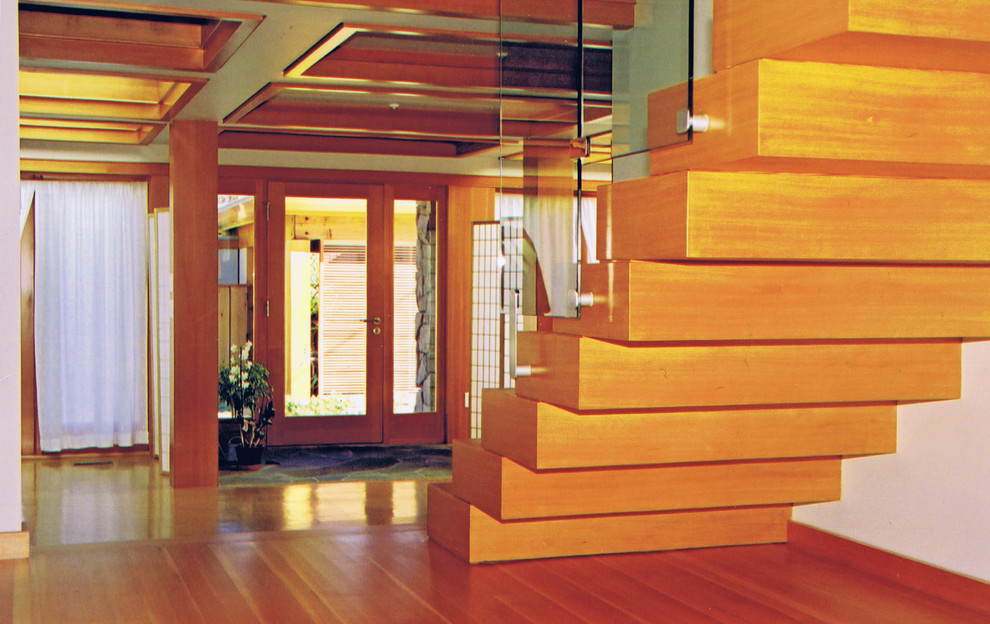 Immagine di una scala sospesa minimal di medie dimensioni con pedata in legno, alzata in legno e parapetto in vetro