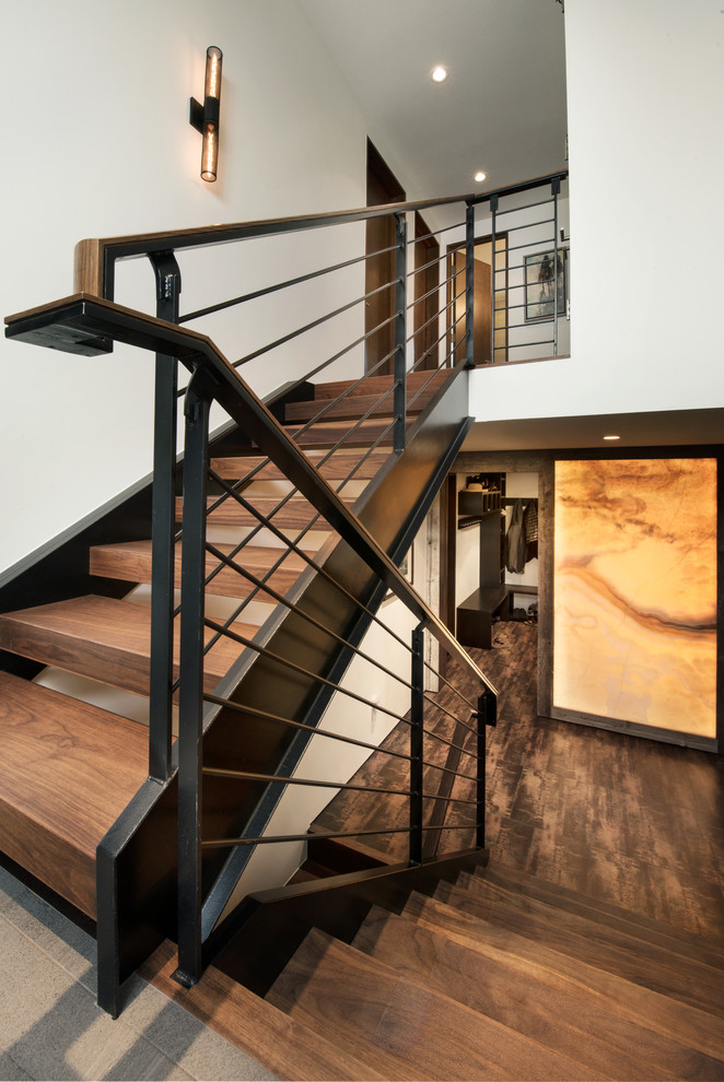 Cette image montre un grand escalier sans contremarche design en U avec des marches en bois et un garde-corps en métal.