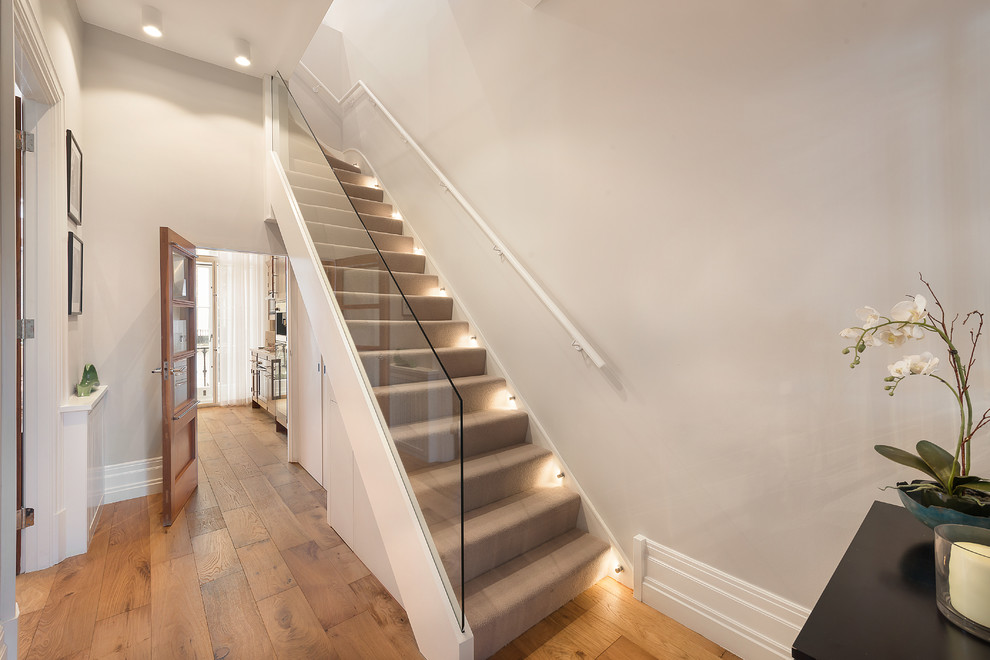 Идея дизайна: лестница в стиле неоклассика (современная классика) с ступенями с ковровым покрытием, ковровыми подступенками и стеклянными перилами