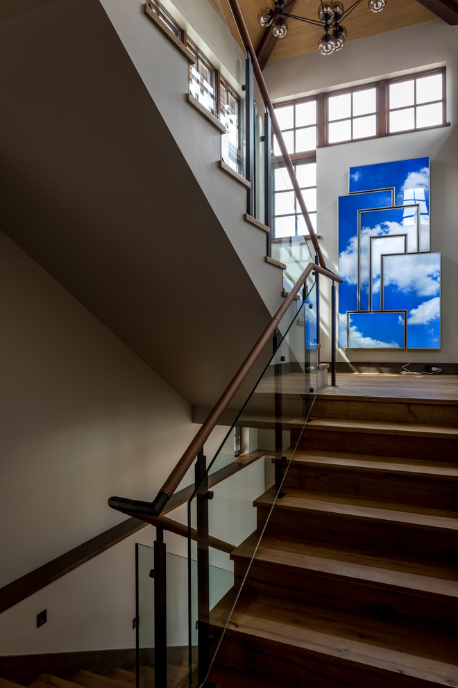 На фото: огромная п-образная деревянная лестница в современном стиле с деревянными ступенями и стеклянными перилами с