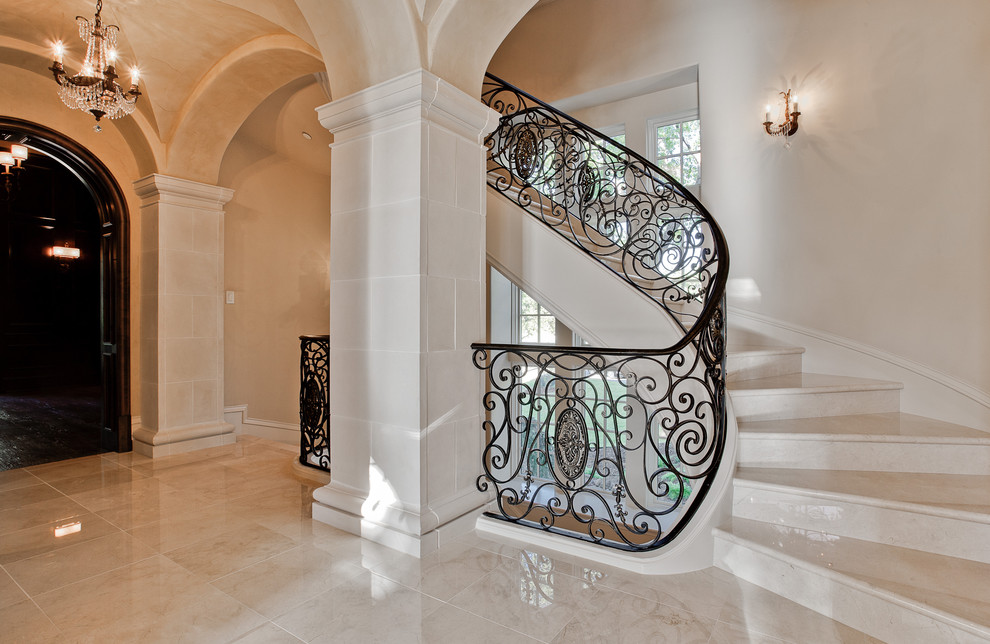 Diseño de escalera curva mediterránea grande con escalones de mármol, contrahuellas de mármol y barandilla de metal