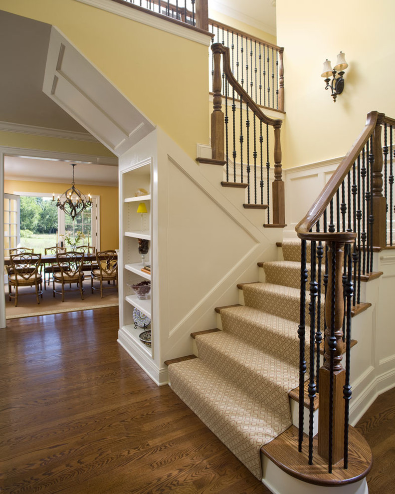 На фото: п-образная лестница в классическом стиле с деревянными ступенями, ковровыми подступенками, перилами из смешанных материалов и кладовкой или шкафом под ней