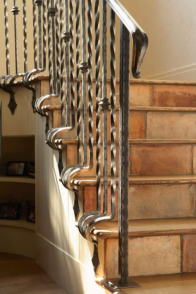 Cette image montre un escalier traditionnel avec des contremarches en terre cuite, un garde-corps en métal et des marches en bois.