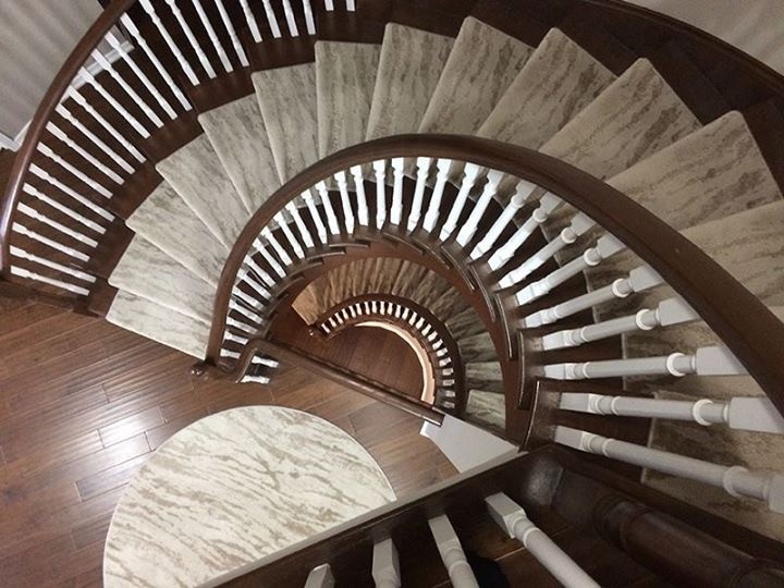 На фото: огромная изогнутая лестница в классическом стиле с ступенями с ковровым покрытием, ковровыми подступенками и деревянными перилами с