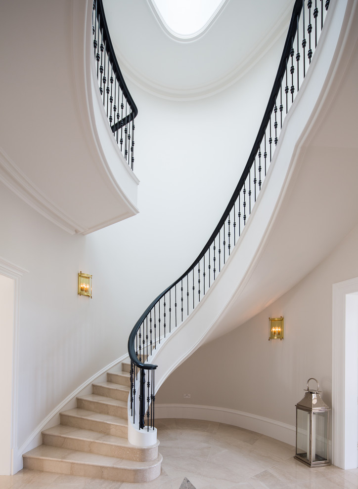 Cette image montre un très grand escalier courbe traditionnel en marbre avec des contremarches en marbre et un garde-corps en métal.