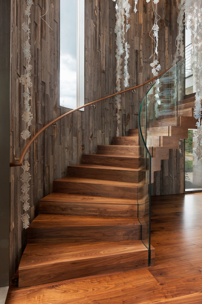Modelo de escalera curva rústica con escalones de madera, contrahuellas de madera y barandilla de vidrio