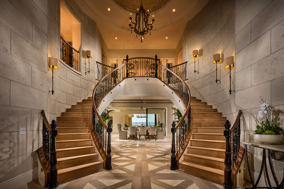 На фото: огромная изогнутая деревянная лестница в средиземноморском стиле с деревянными ступенями и металлическими перилами с