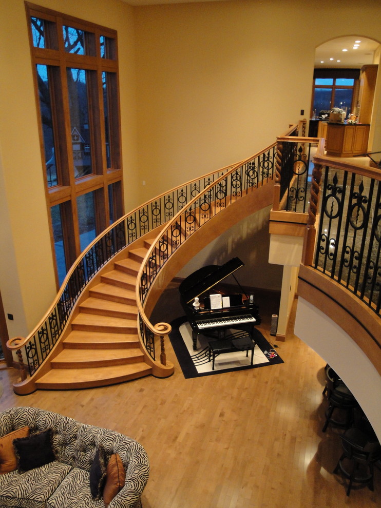 Стильный дизайн: огромная изогнутая деревянная лестница в стиле фьюжн с деревянными ступенями - последний тренд