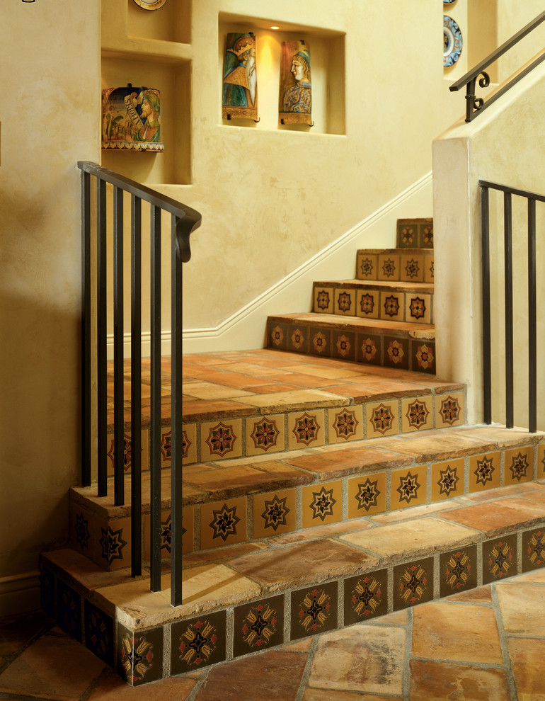 Foto de escalera mediterránea con escalones de terracota, contrahuellas con baldosas y/o azulejos y barandilla de metal