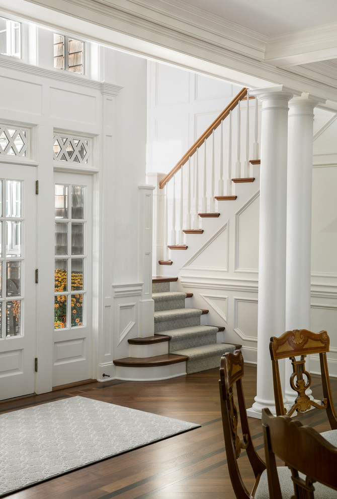Стильный дизайн: огромная угловая деревянная лестница в стиле неоклассика (современная классика) с деревянными ступенями и деревянными перилами - последний тренд