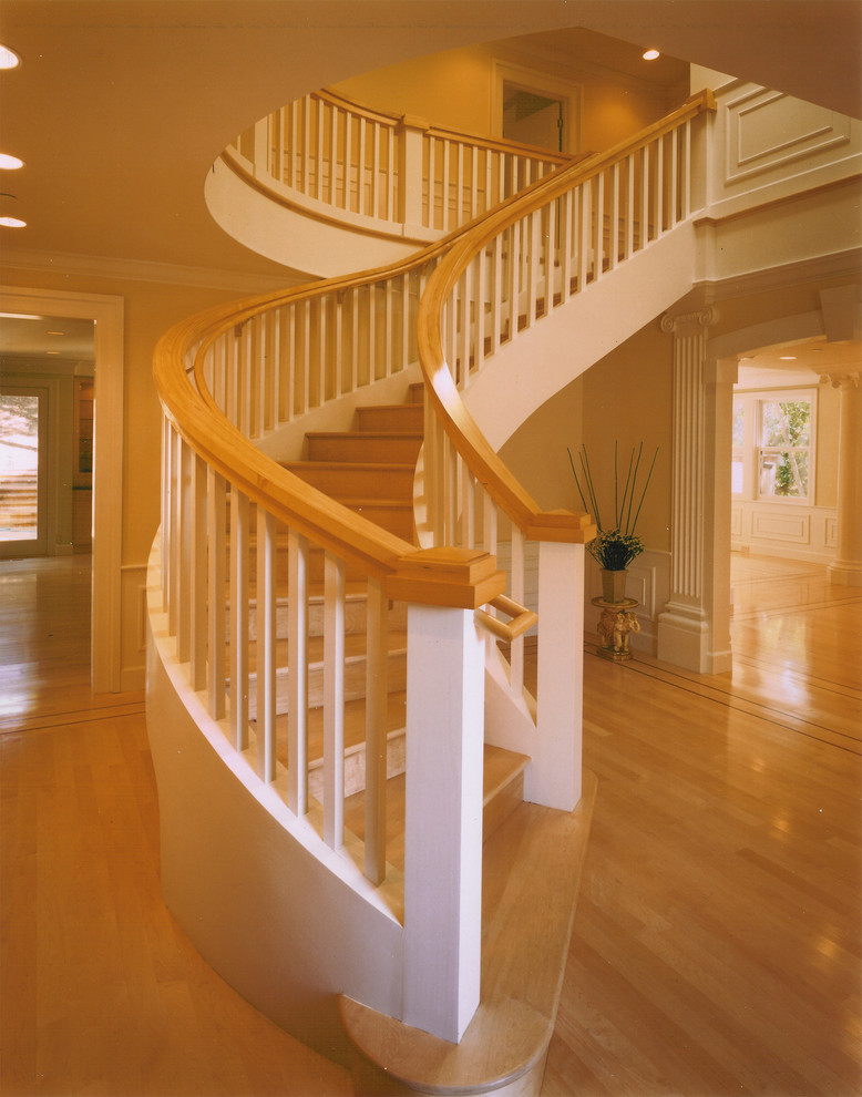 На фото: огромная изогнутая деревянная лестница в классическом стиле с деревянными ступенями и деревянными перилами