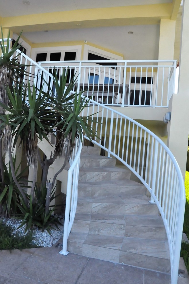 Imagen de escalera curva grande con barandilla de metal, escalones con baldosas y contrahuellas con baldosas y/o azulejos
