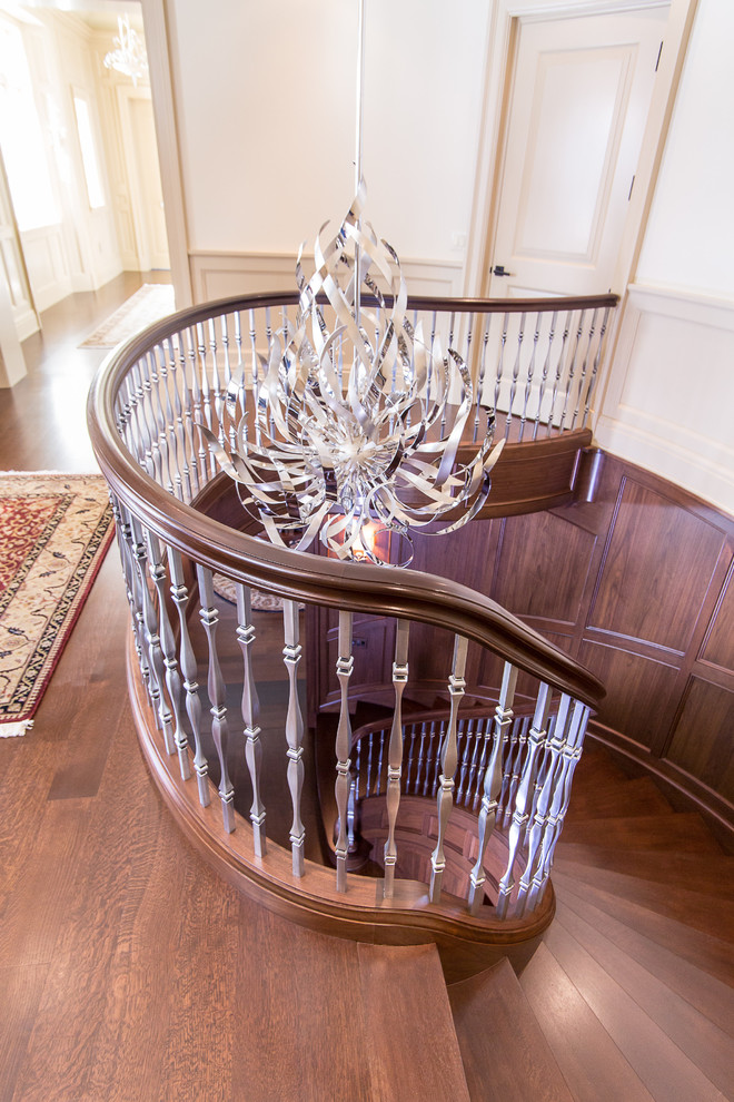 Стильный дизайн: огромная изогнутая деревянная лестница в классическом стиле с деревянными ступенями - последний тренд