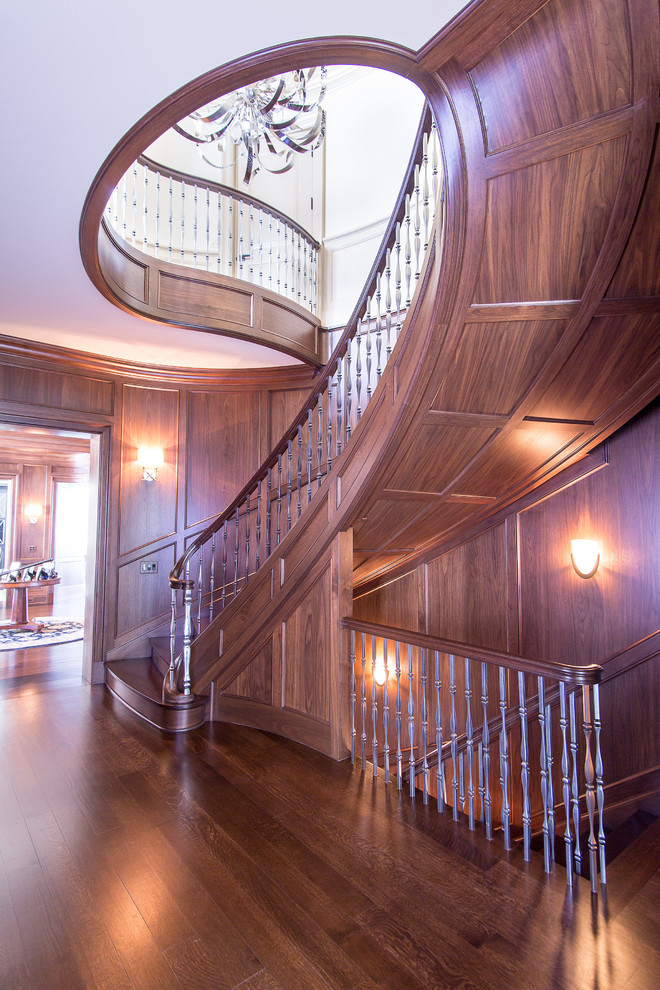На фото: огромная изогнутая деревянная лестница в классическом стиле с деревянными ступенями с