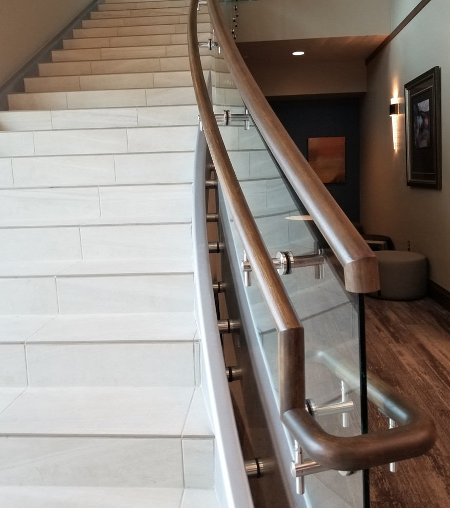 Cette photo montre un grand escalier carrelé courbe tendance avec des contremarches carrelées et un garde-corps en verre.