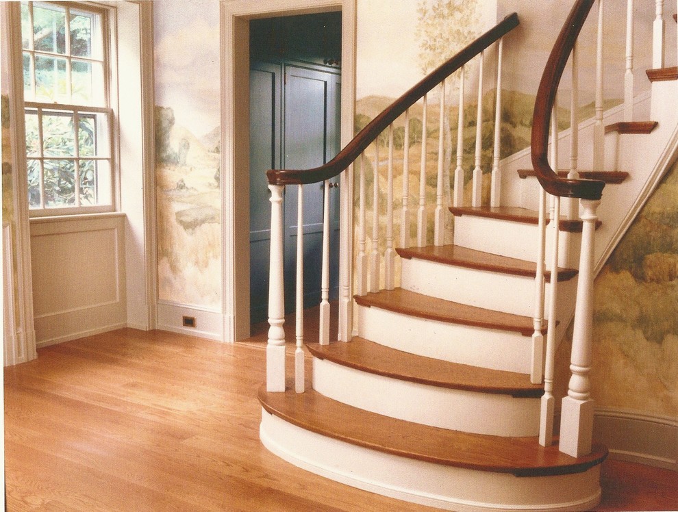 Diseño de escalera curva de estilo de casa de campo grande con escalones de madera y contrahuellas de madera pintada