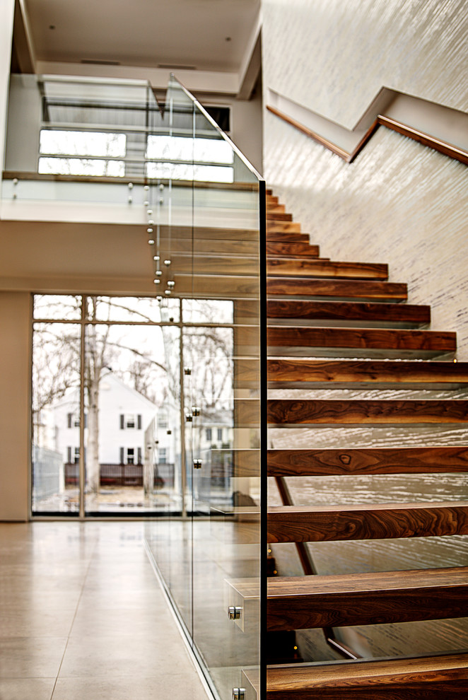 Exempel på en modern flytande trappa i trä, med räcke i glas och öppna sättsteg