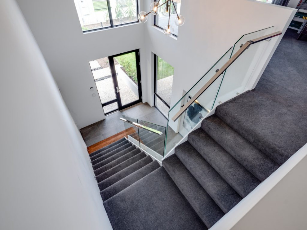 Идея дизайна: угловая лестница с ступенями с ковровым покрытием, стеклянными подступенками и стеклянными перилами
