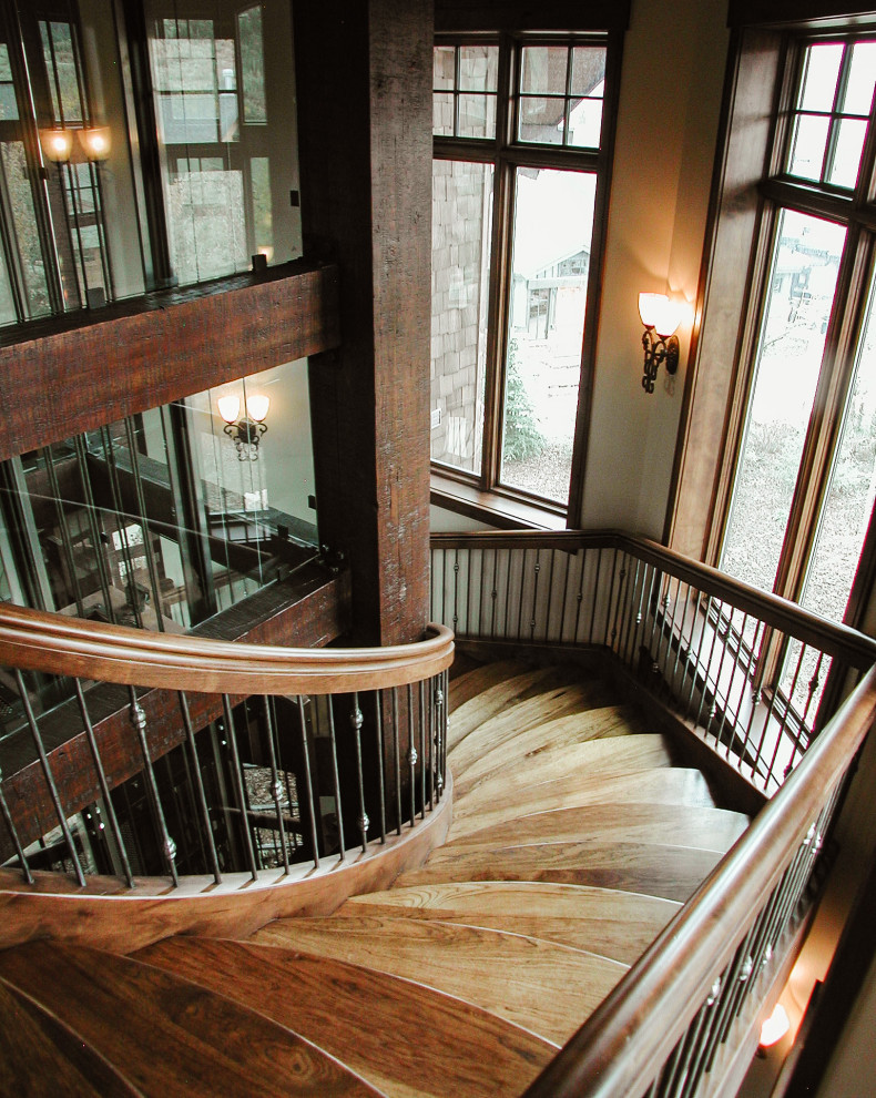 Réalisation d'un grand escalier sans contremarche courbe tradition avec des marches en bois et un garde-corps en métal.