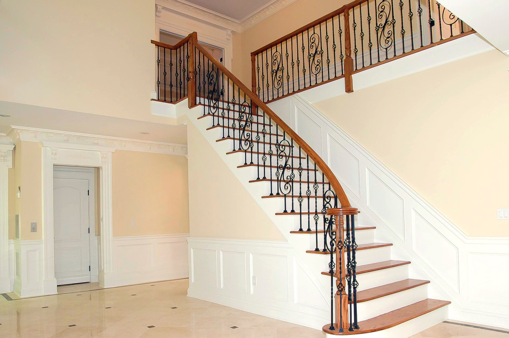 Large elegant wooden curved staircase photo in New York with painted risers