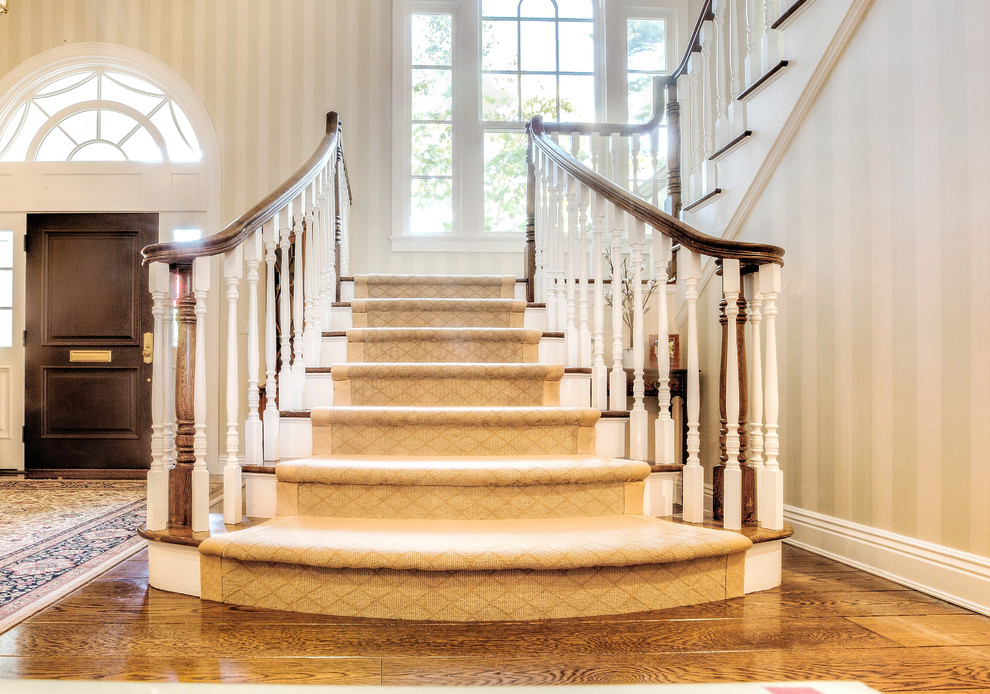 Пример оригинального дизайна: большая п-образная лестница в классическом стиле с деревянными ступенями и крашенными деревянными подступенками
